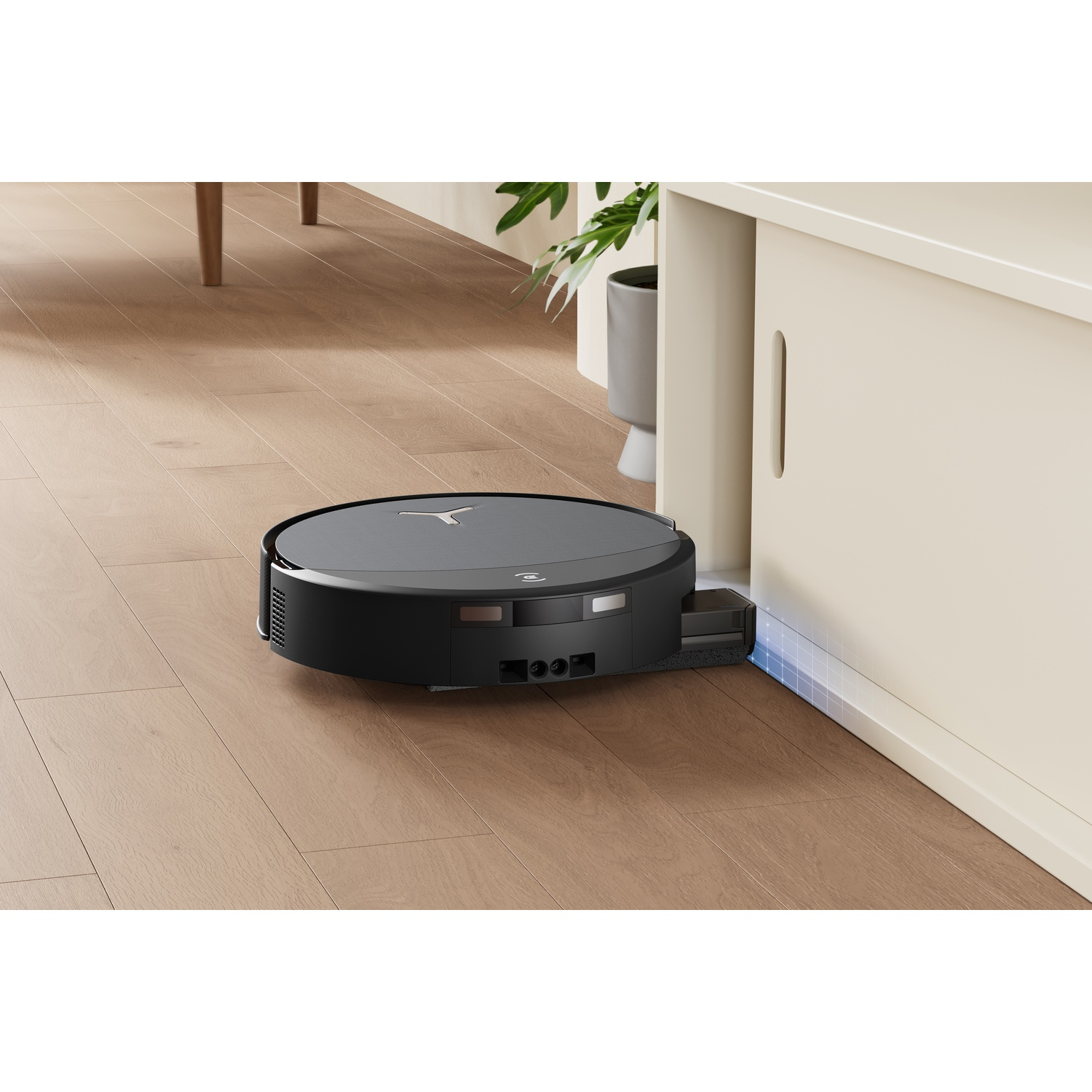 Un robot aspirapolvere nero si muove su un pavimento in legno in una nicchia bianca.