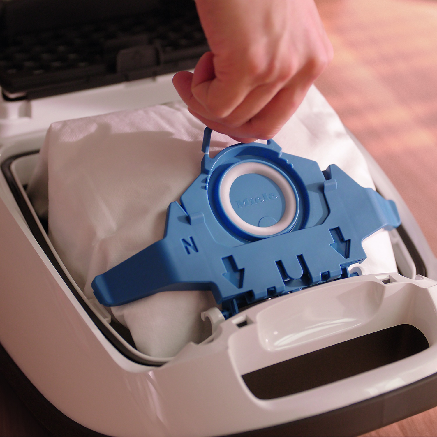 Una mano inserisce un sacchetto polvere Miele blu in un aspirapolvere bianco.
