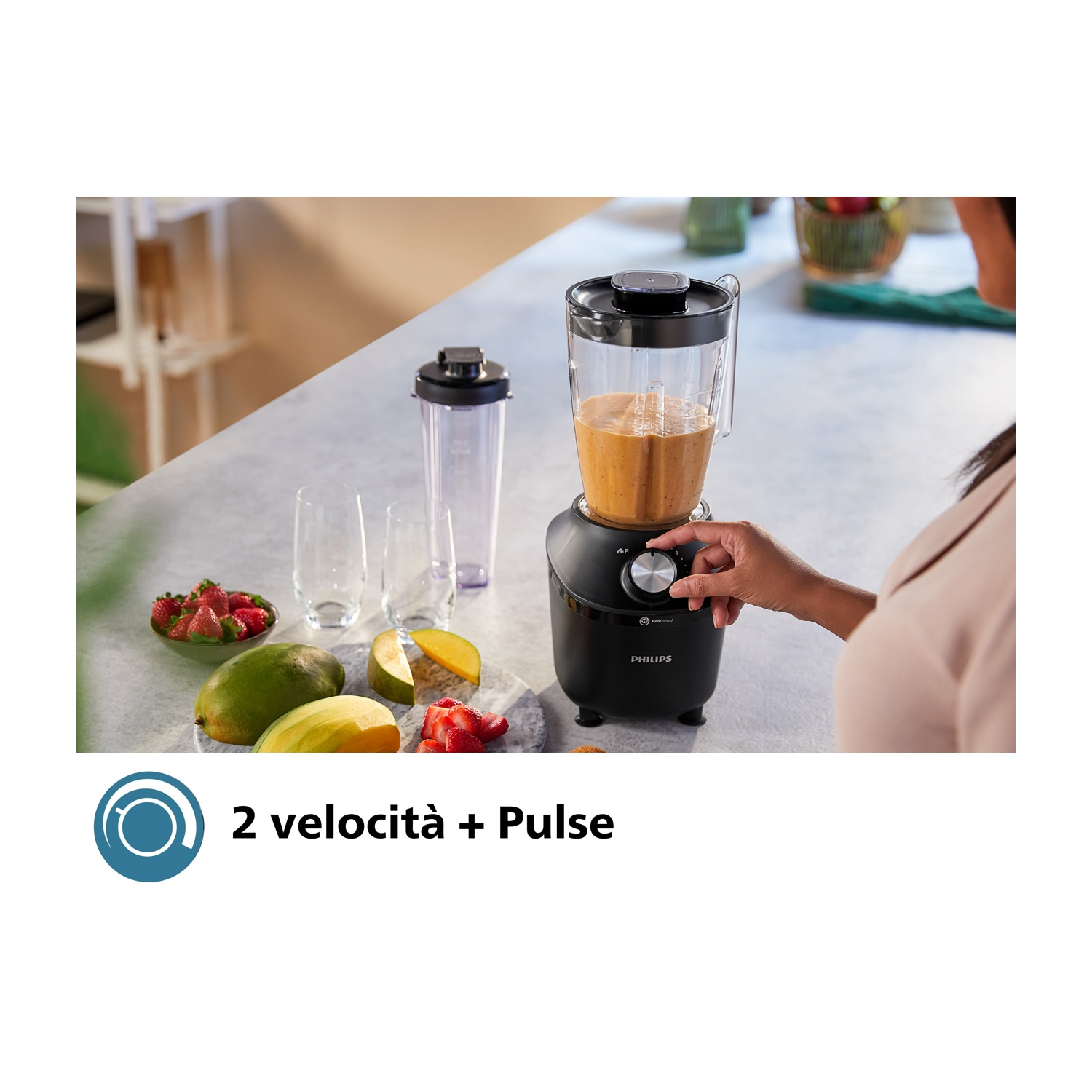Frullatore nero con frutta: fragole, mango. Una mano regola l'impostazione di velocità.