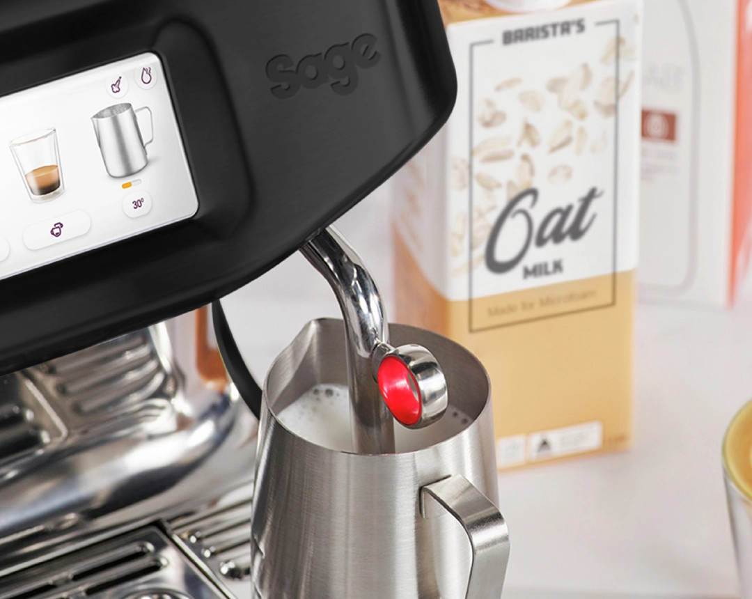 Ekspres do kawy Sage spienia mleko w dzbanku obok kartonu mleka owsianego.