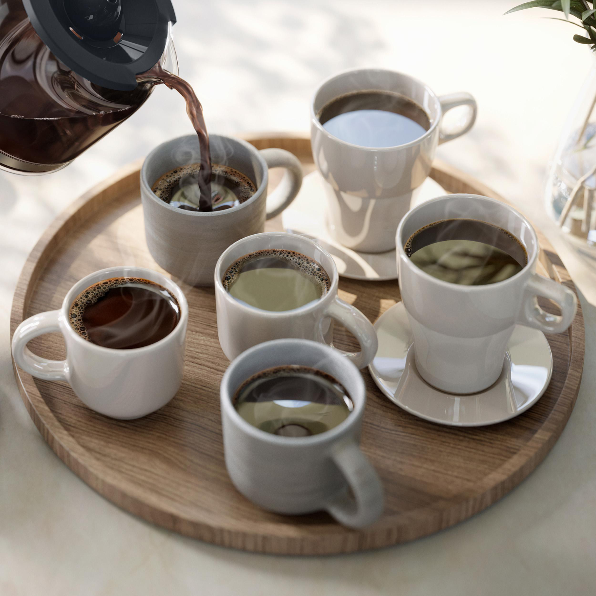 Kaffeekanne gießt Kaffee in mehrere Tassen auf einem Holzteller.