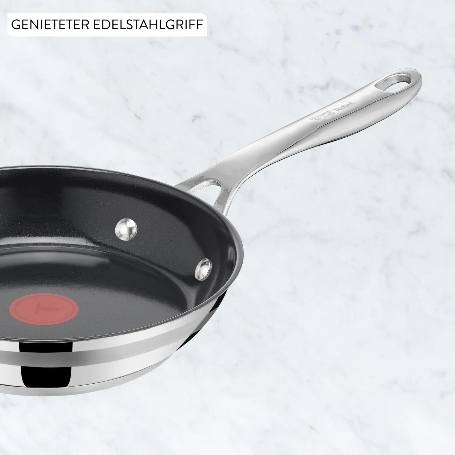 Eine silberne Bratpfanne mit schwarzem Innenraum und rotem Logo auf Marmor.