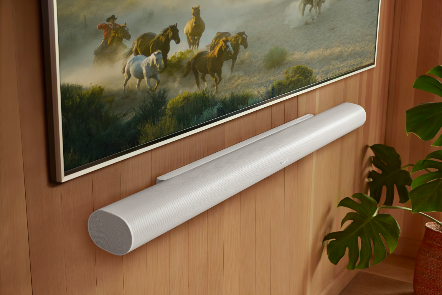 Una barra de sonido blanca cuelga de una pared de madera debajo de un televisor con caballos.