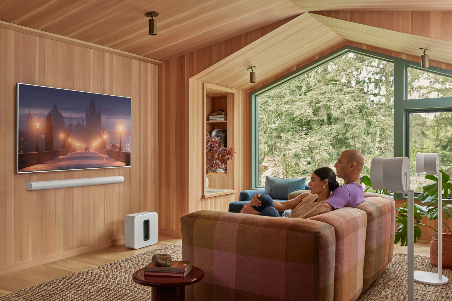Una pareja se relaja en un sofá en una sala con paneles de madera con vistas a un jardín.