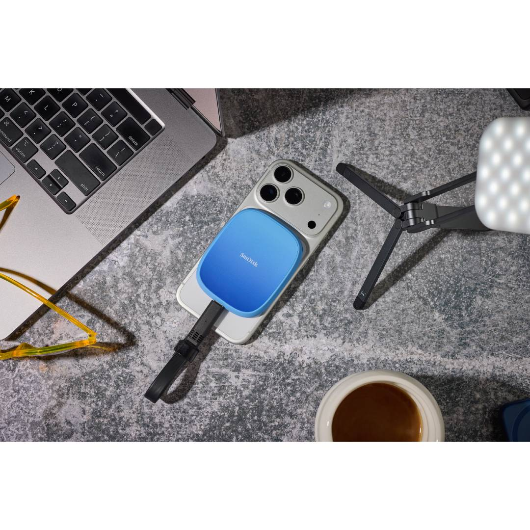 Una unidad azul SanDisk está conectada a un iPhone, junto a un portátil.