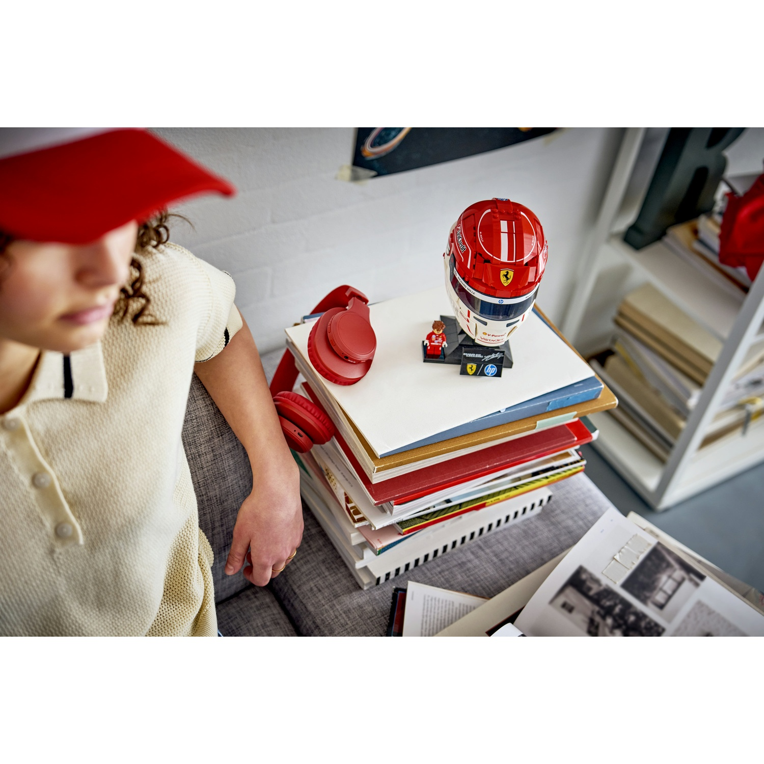 Un bambino con cappellino rosso siede vicino a una pila di libri con un casco Ferrari.