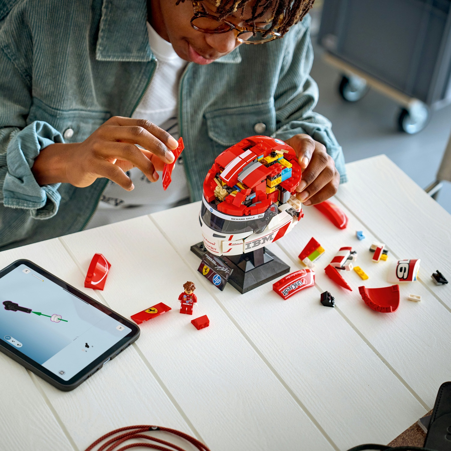 Una persona sta costruendo un casco Lego rosso e bianco, con pezzi sparsi su un tavolo bianco.