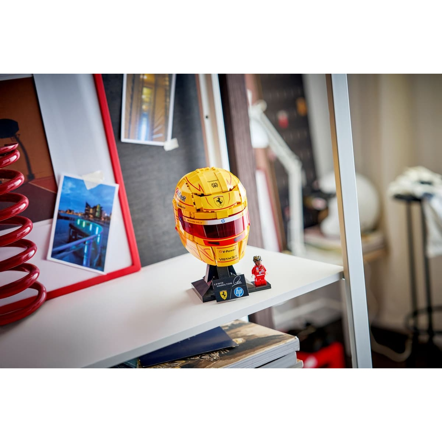 Modello di casco F1 giallo con visiera rossa su supporto, piccola figura accanto.