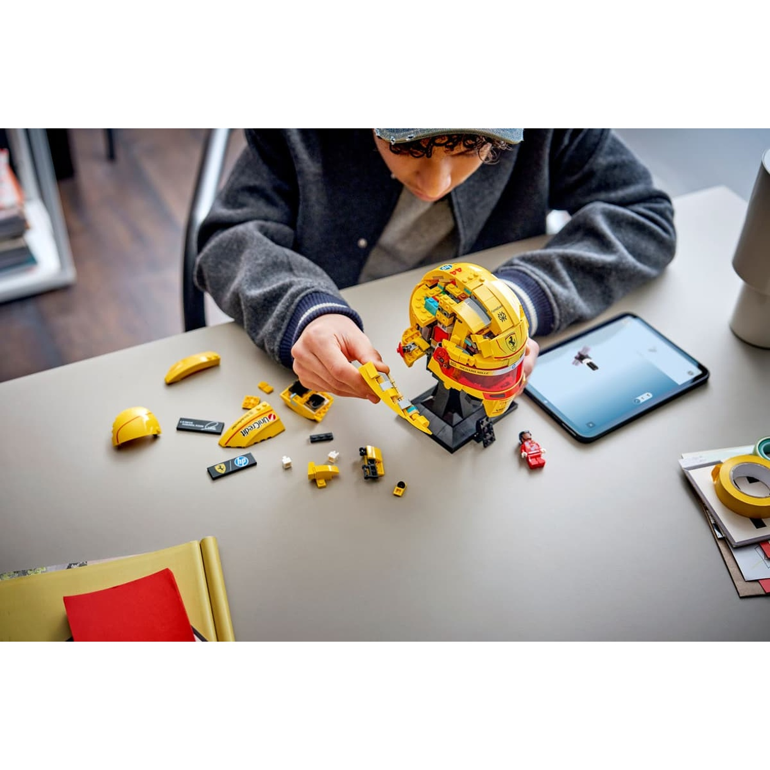 Un bambino costruisce un casco Ferrari giallo con mattoncini Lego, con pezzi sparsi.
