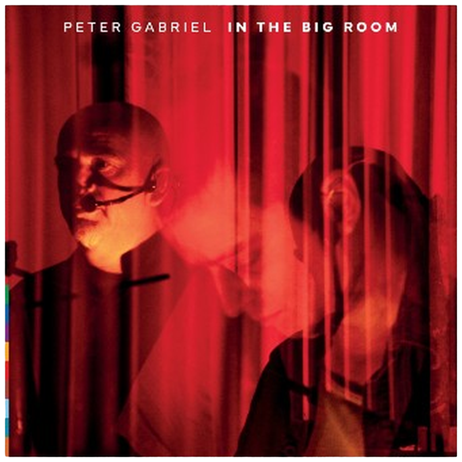 Peter Gabriel avec micro et rideau rouge éclairé. Deux silhouettes visibles.