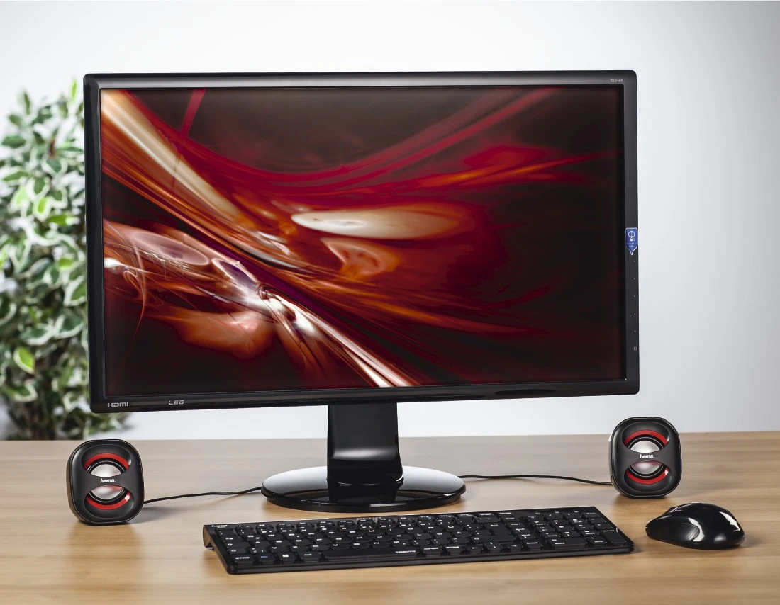 Un moniteur, un clavier, une souris et deux haut-parleurs sur un bureau en bois.