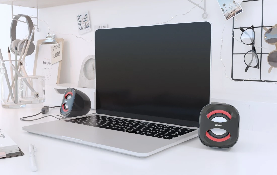 Un ordinateur portable avec des haut-parleurs, des écouteurs et des stylos sur un bureau.