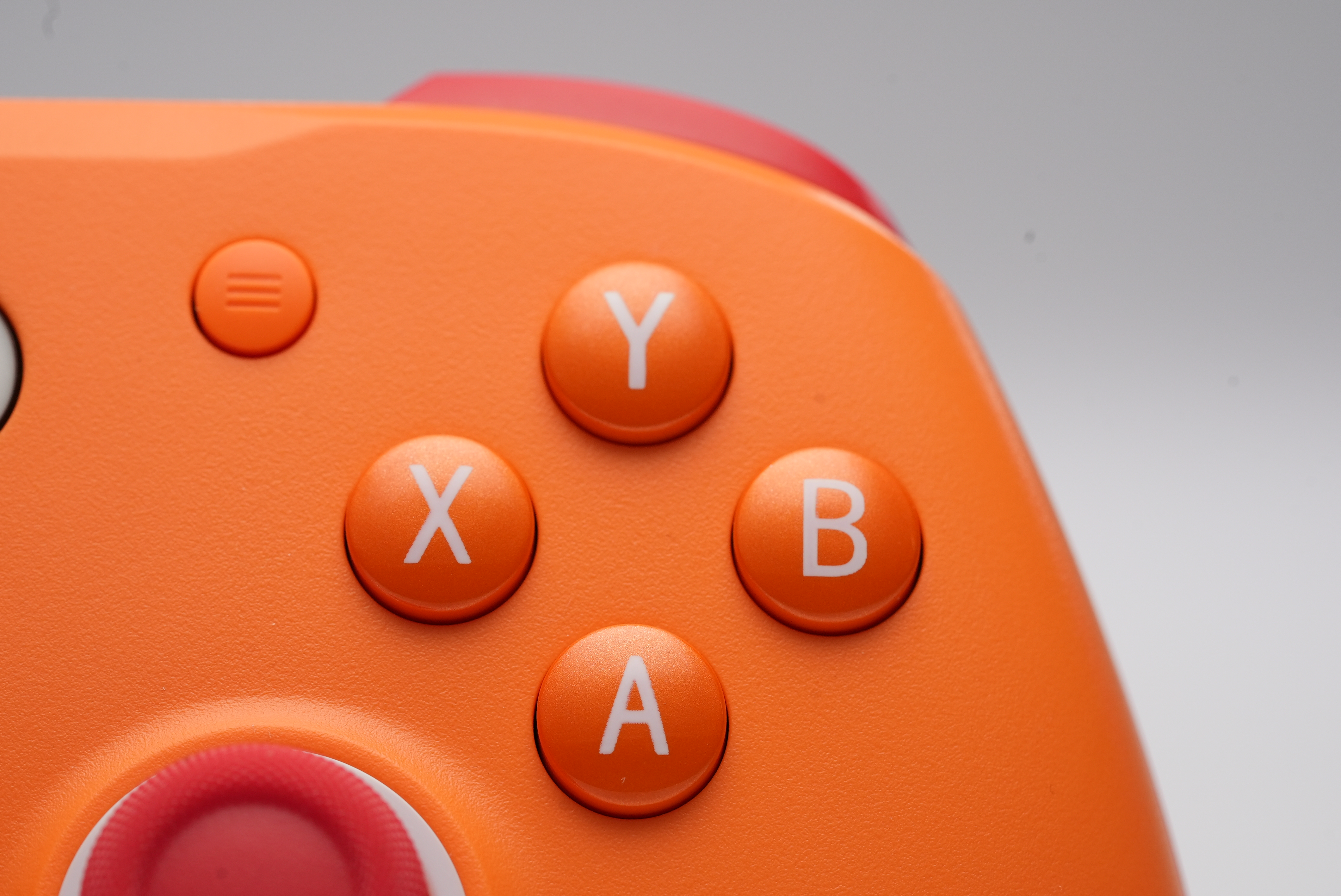 Orange Controller-Tasten A, B, X, Y und Menü-Symbol auf grauem Hintergrund.