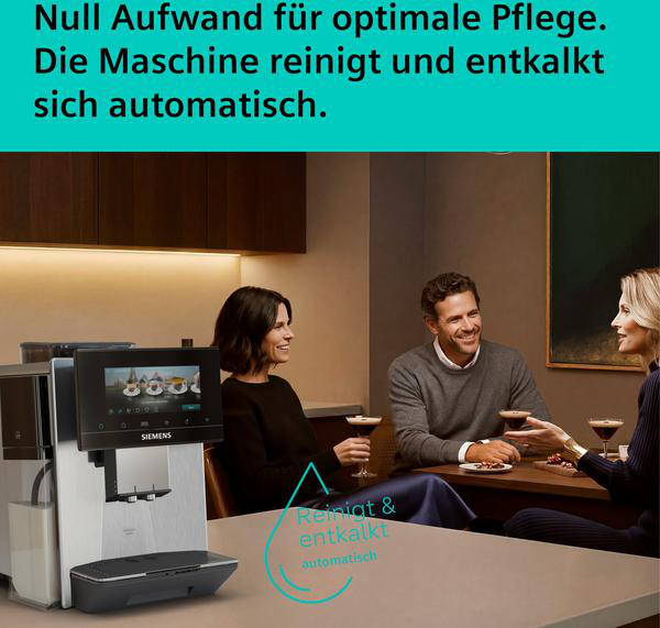 Ein Kaffeevollautomat mit Touchscreen steht auf einer Arbeitsplatte, daneben sitzen drei Personen.