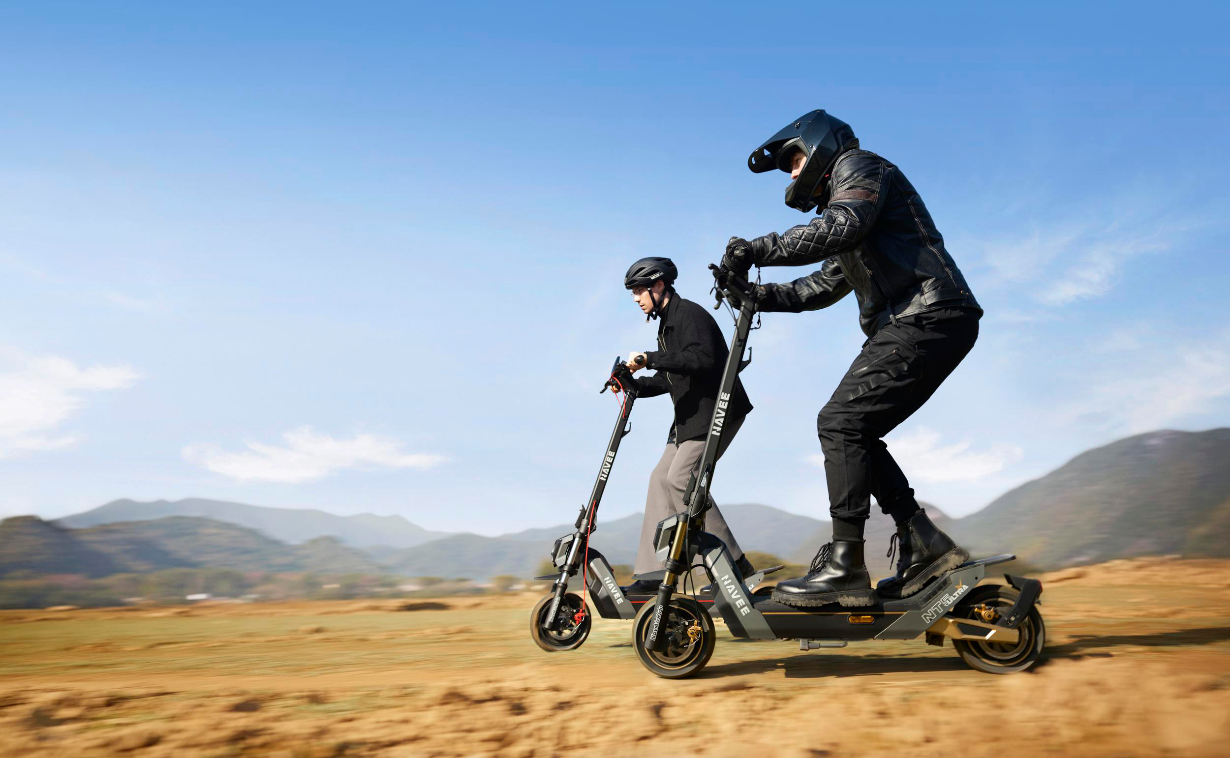 Zwei Personen auf E-Scootern fahren in einer bergigen Landschaft.