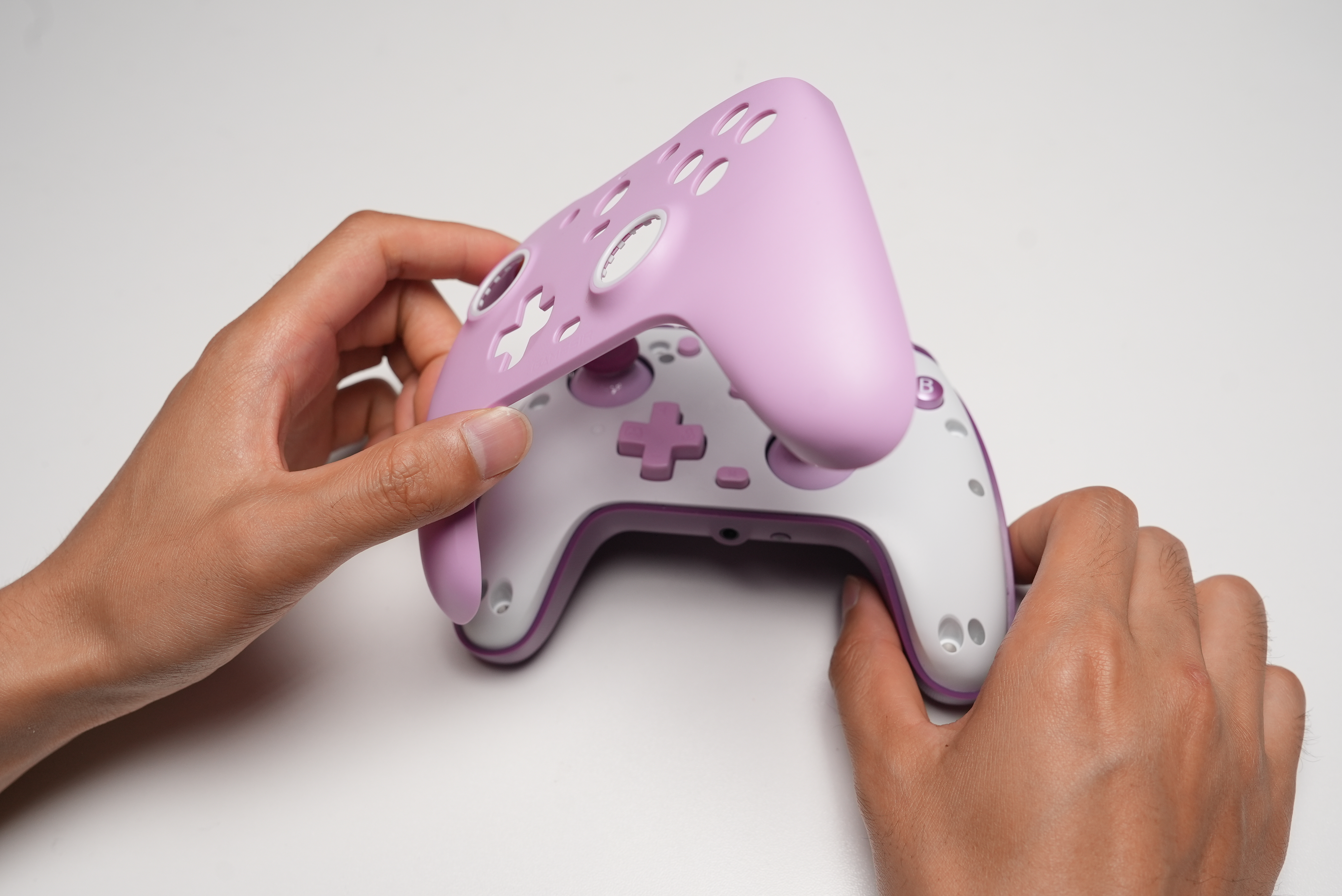 Hände halten einen weißen und violetten Controller mit einem hellrosa Aufsatz.
