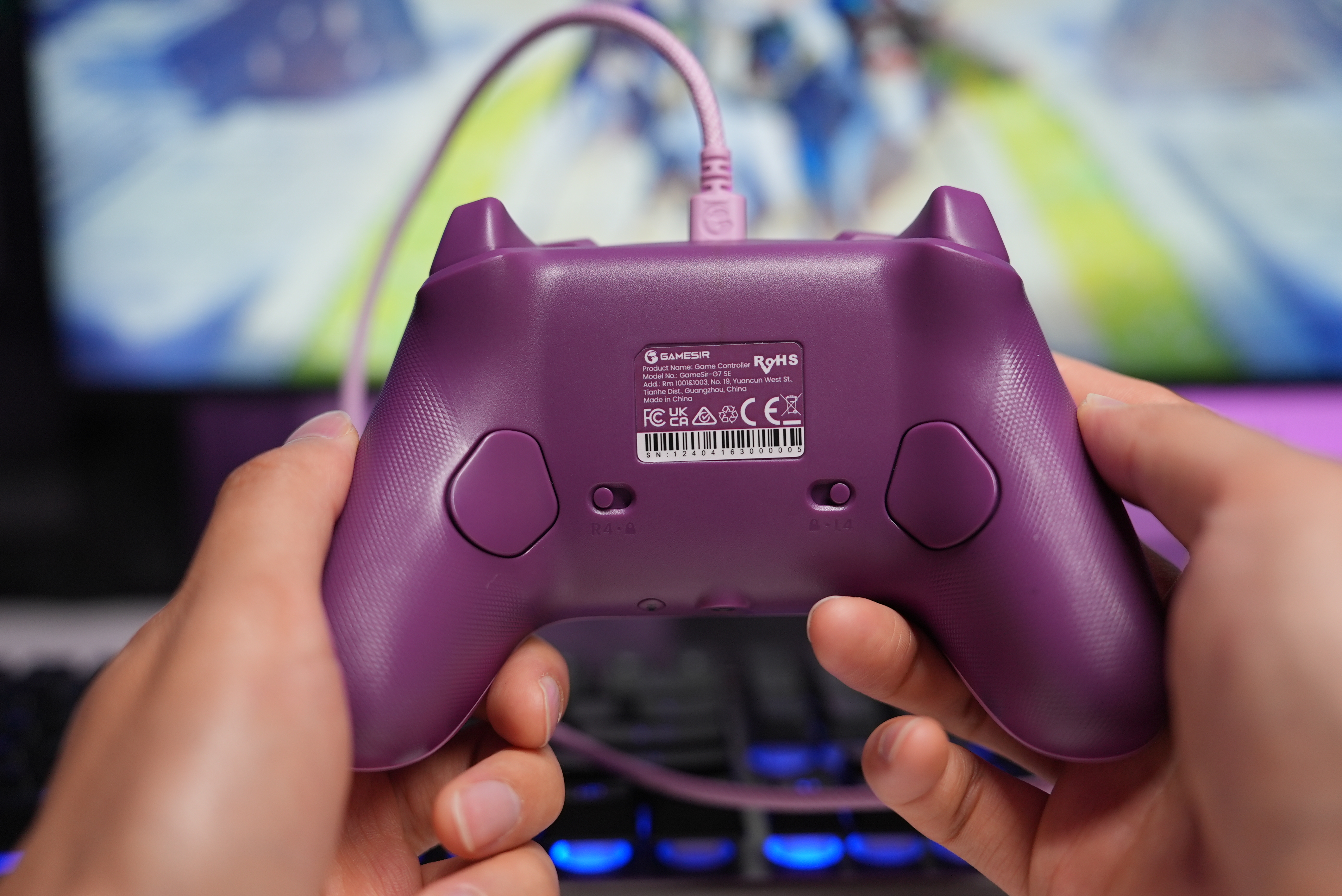 Lila Gamecontroller wird von Händen gehalten, mit Kabel und Beschriftung.