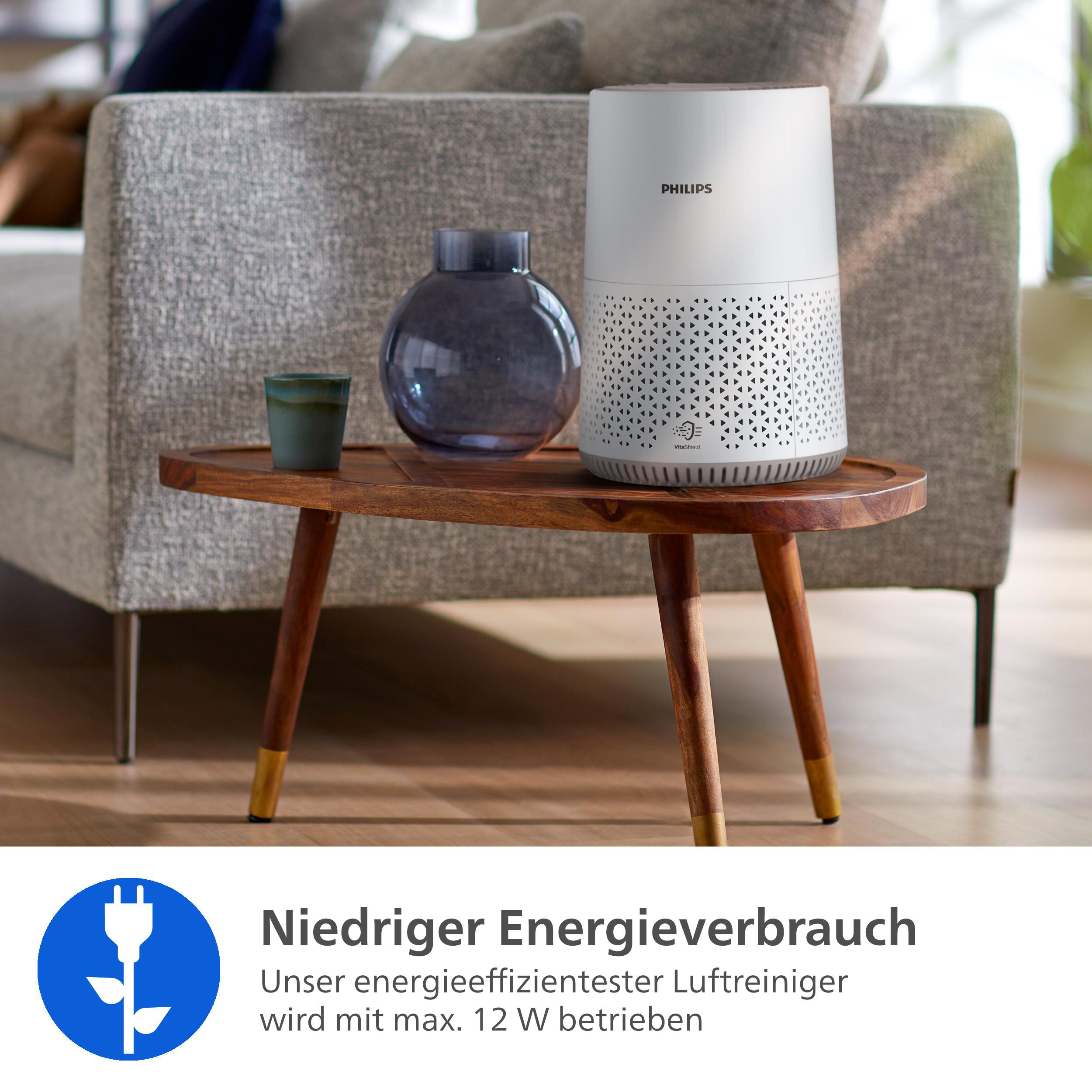 Ein weißer Philips Luftreiniger steht auf einem Holztisch neben einer Vase.