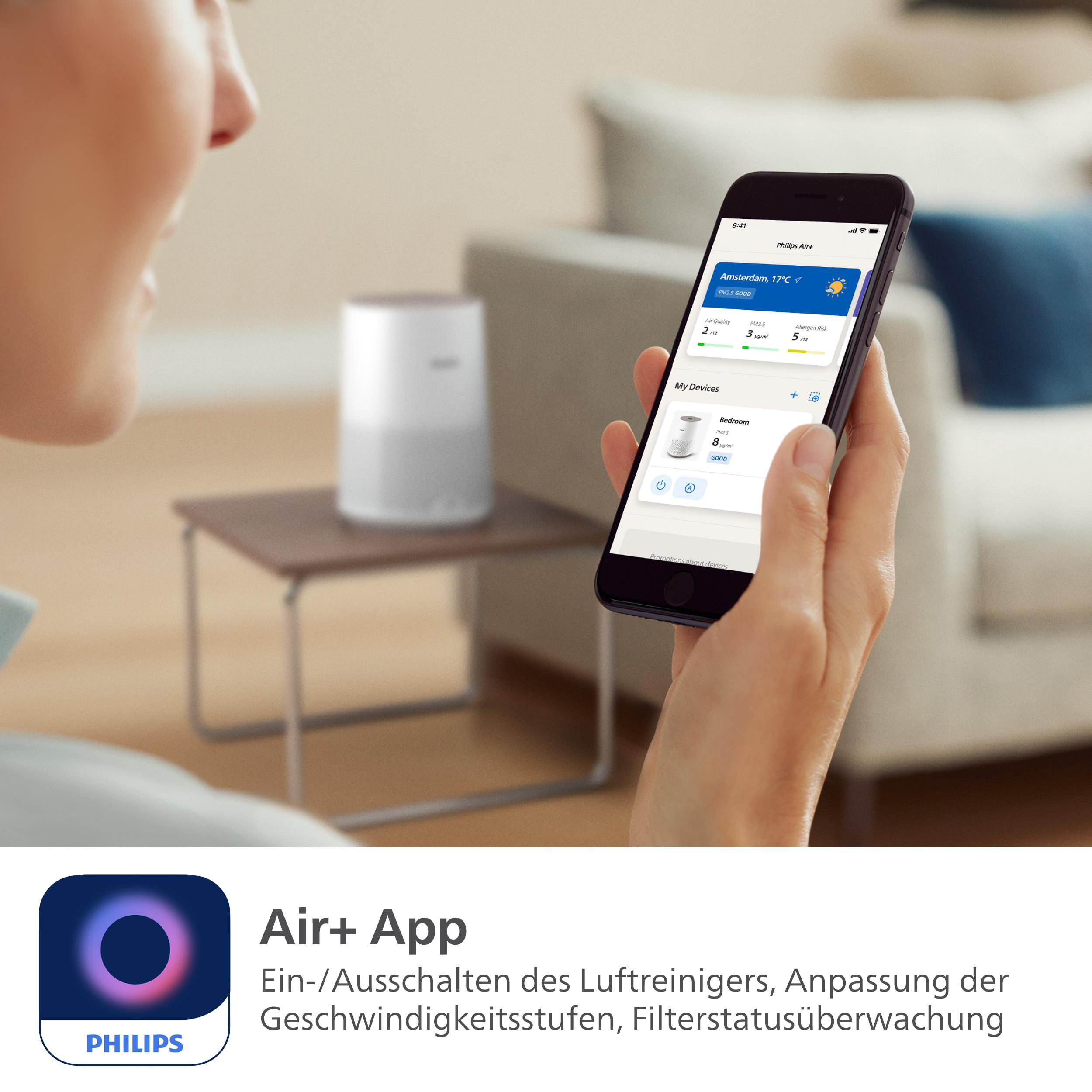 Eine Person hält ein Smartphone mit der Philips Air+ App. Im Hintergrund ein Luftreiniger.