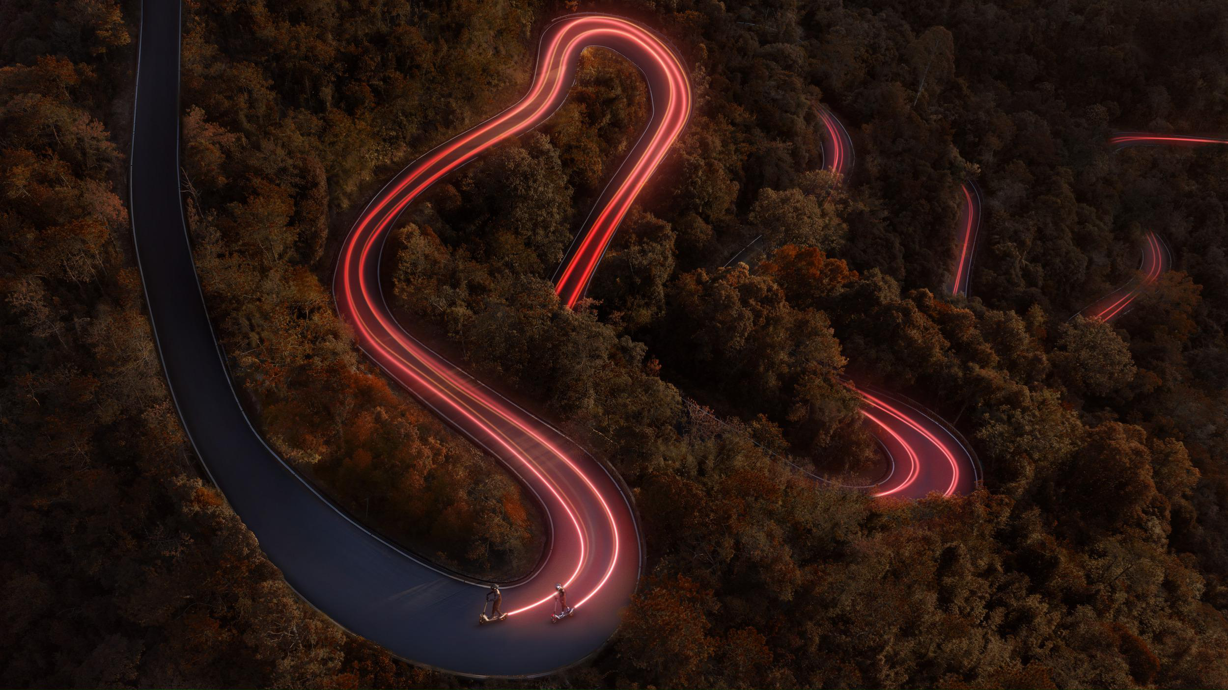 Zwei Roller fahren auf einer kurvigen Straße im Wald bei Nacht. Neonlichtspuren.