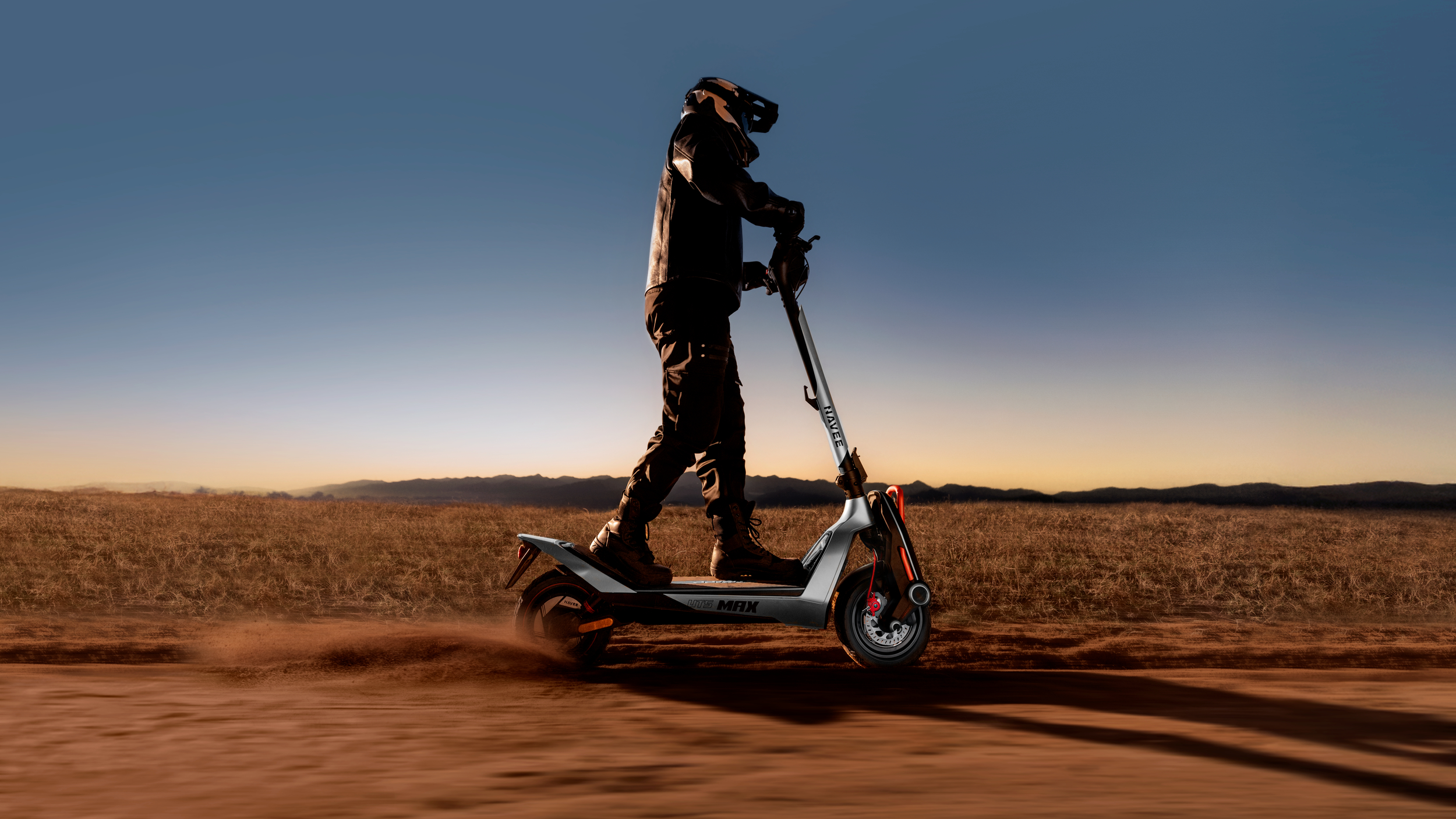 Person fährt E-Scooter in staubiger Landschaft bei Sonnenuntergang.