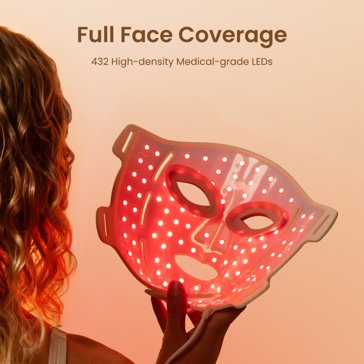 A hand holds a white LED face mask with red lights against an orange background.