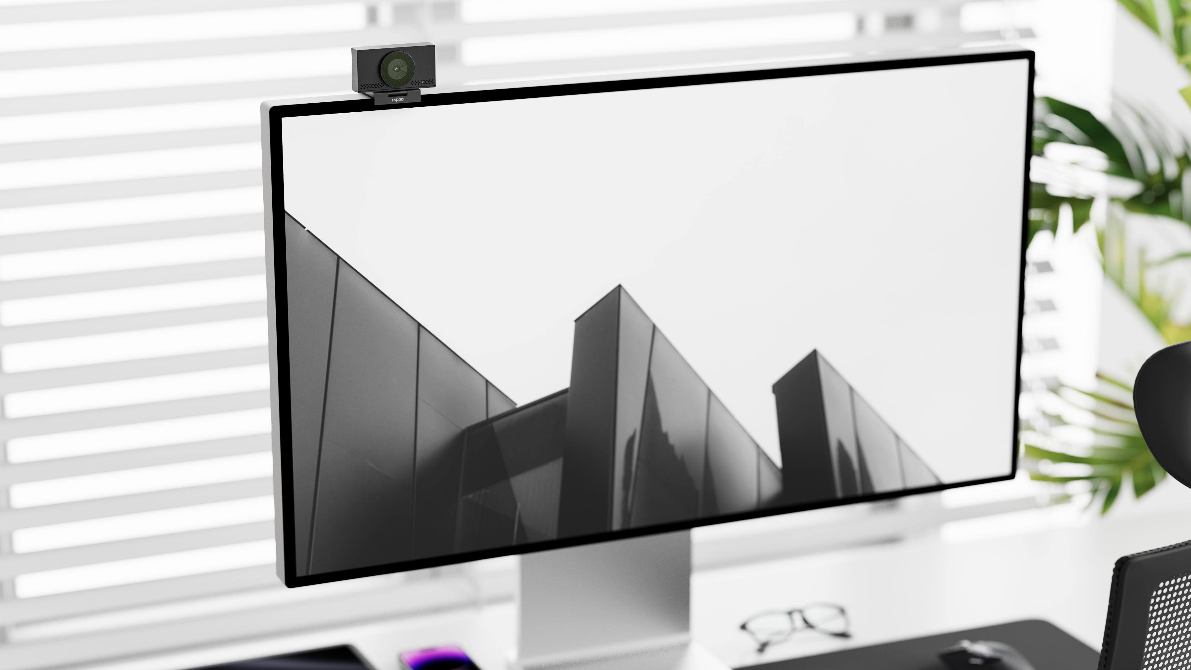 Ein Monitor mit Webcam zeigt eine moderne Gebäudeansicht. Draußen sind Jalousien und Pflanzen.