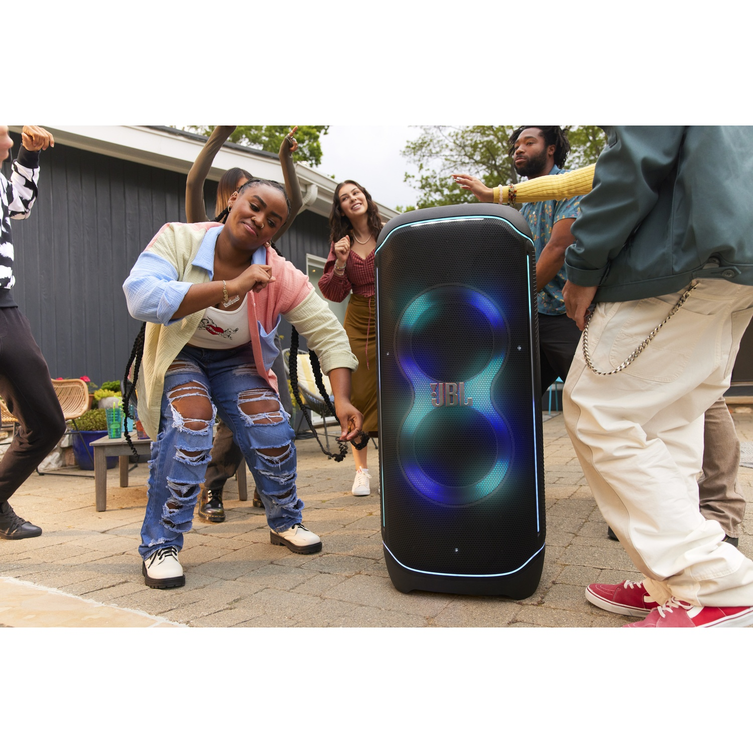 People dance outdoors around a JBL speaker with colorful lights.