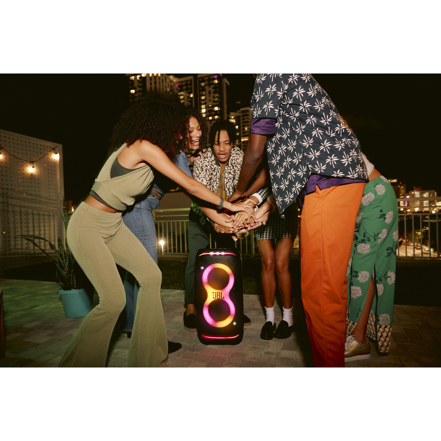 Des amis posent leurs mains sur une enceinte JBL lumineuse lors d'une fête nocturne.