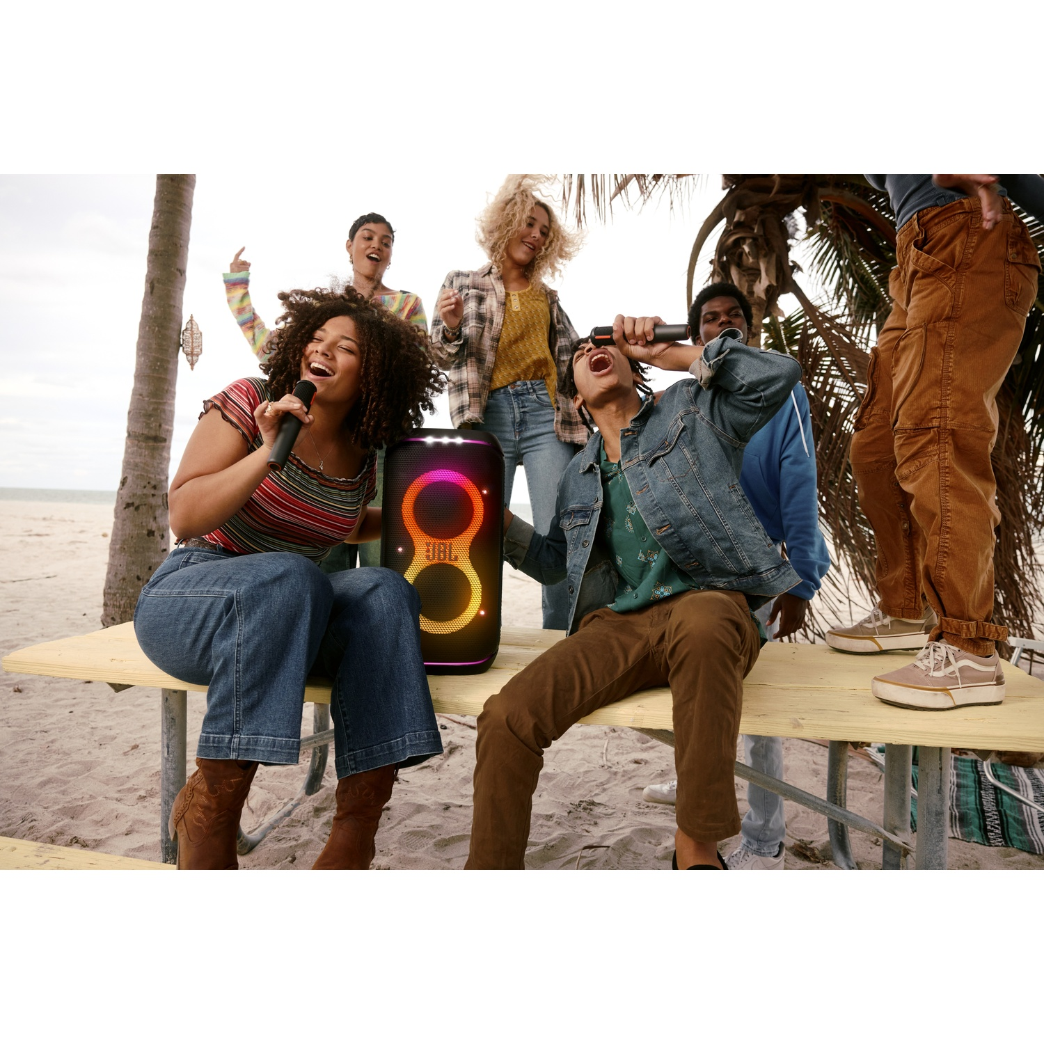 Groep zingt op strand met JBL speaker en microfoons.