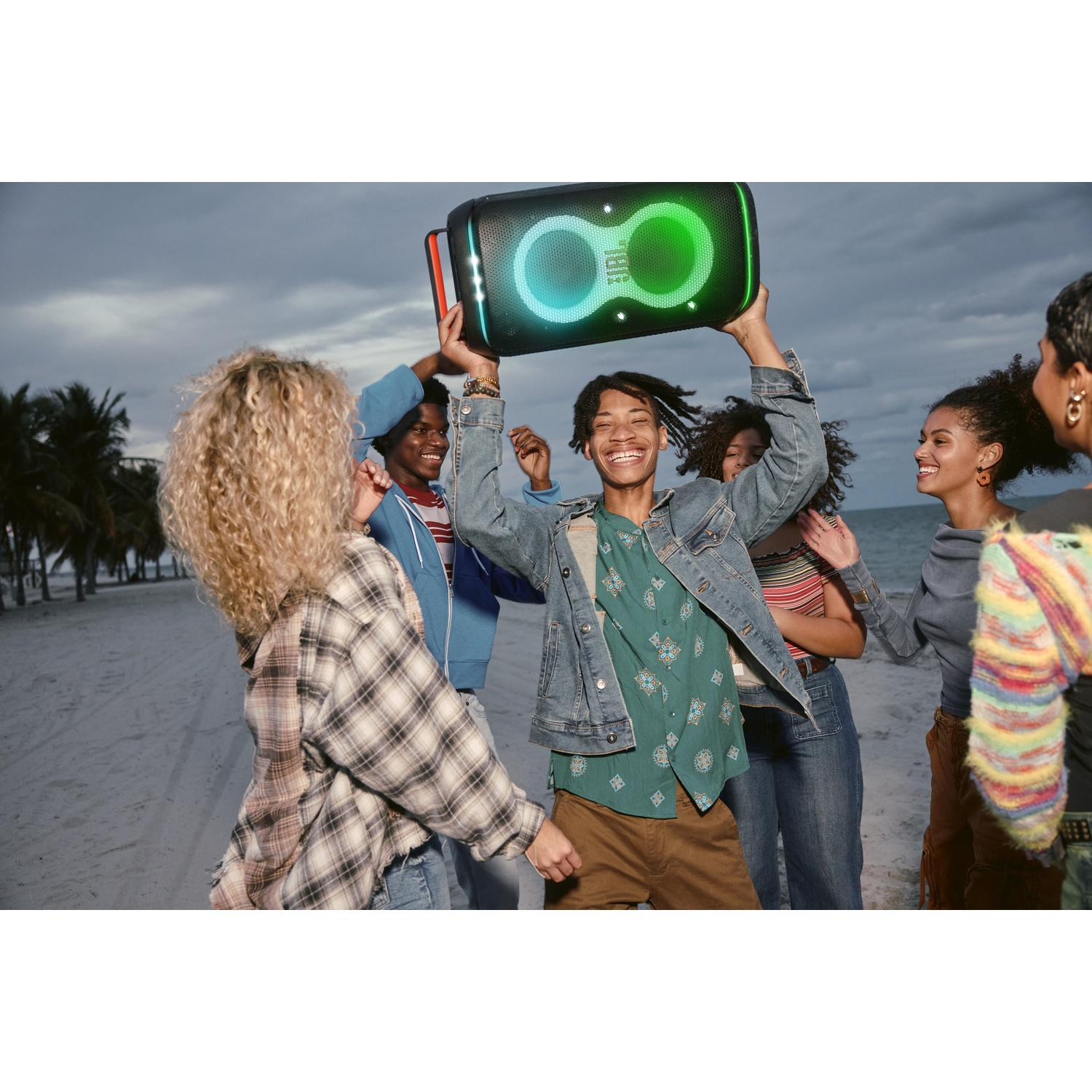 Mensen dansend op een strand met een verlichte speaker in de nacht.