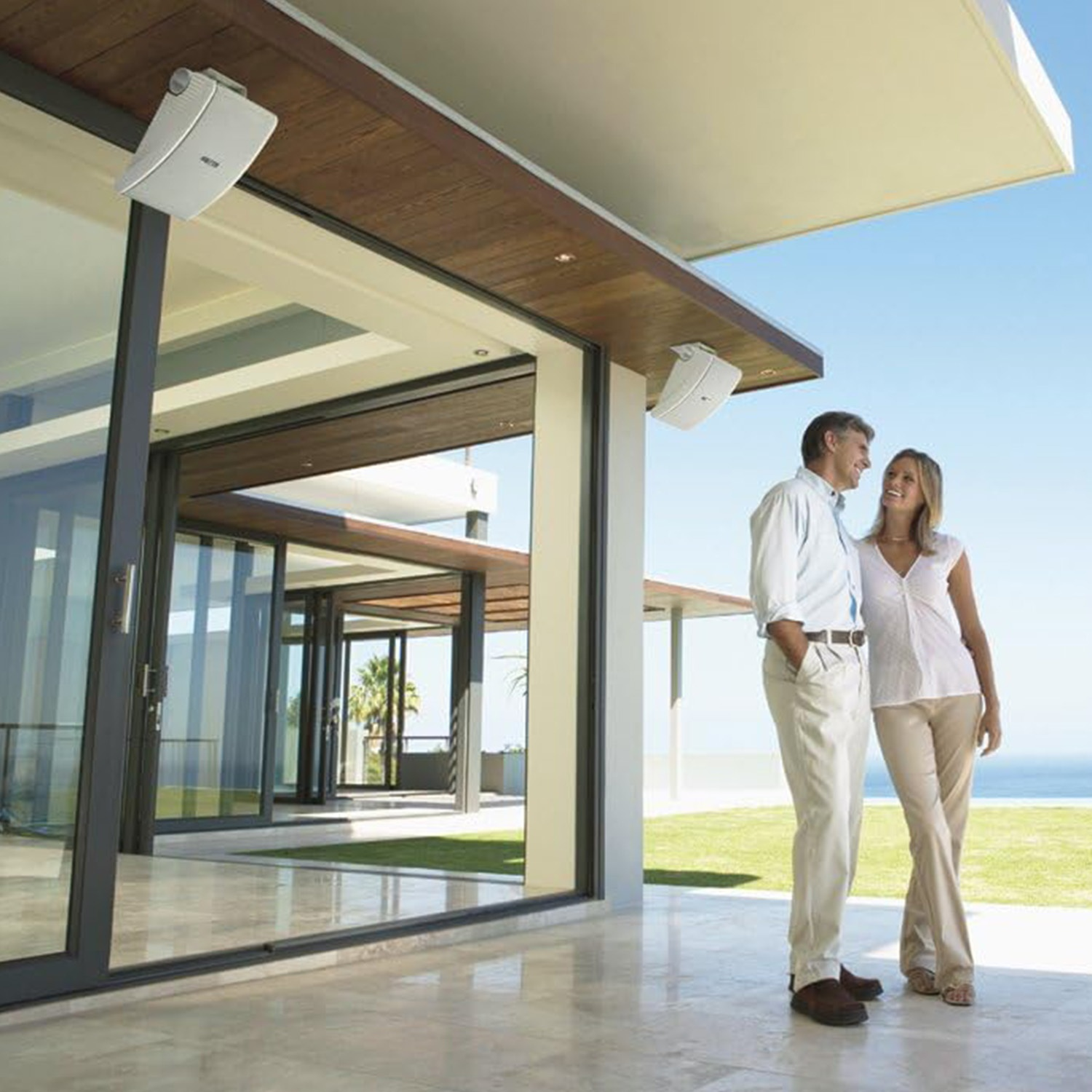Una coppia davanti a una casa moderna con facciata in vetro e vista mare.