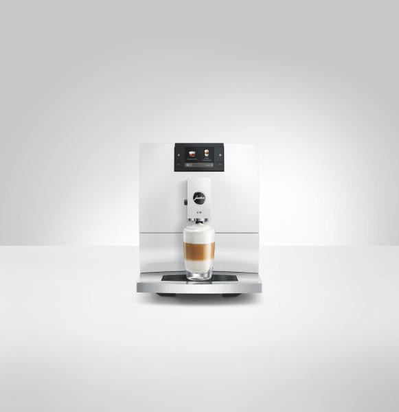Eine weiße Kaffeemaschine mit einem Glas Latte Macchiato steht vorne.