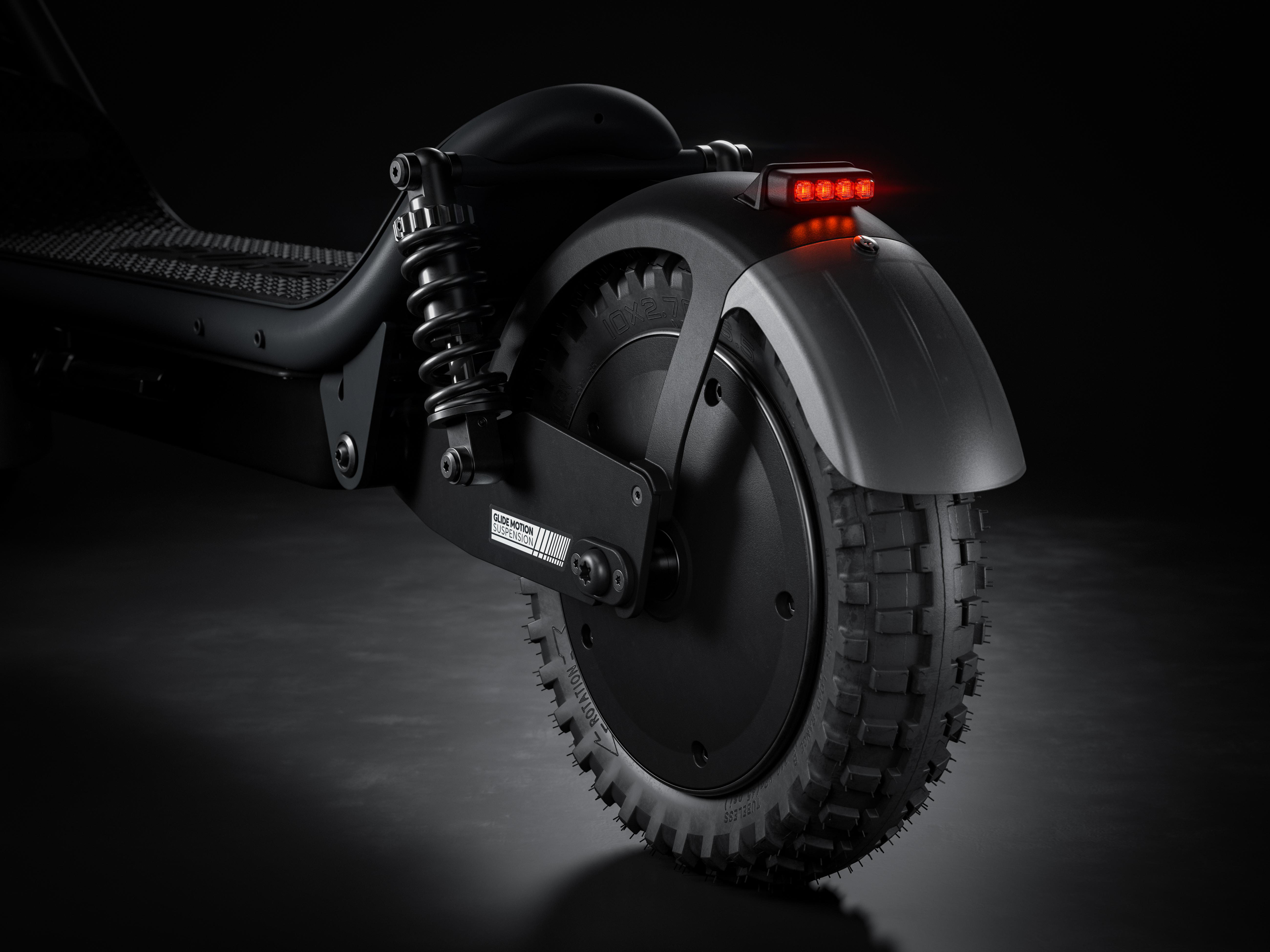 Ein schwarzer E-Scooter-Hinterrad mit Federung und rotem Rücklicht.