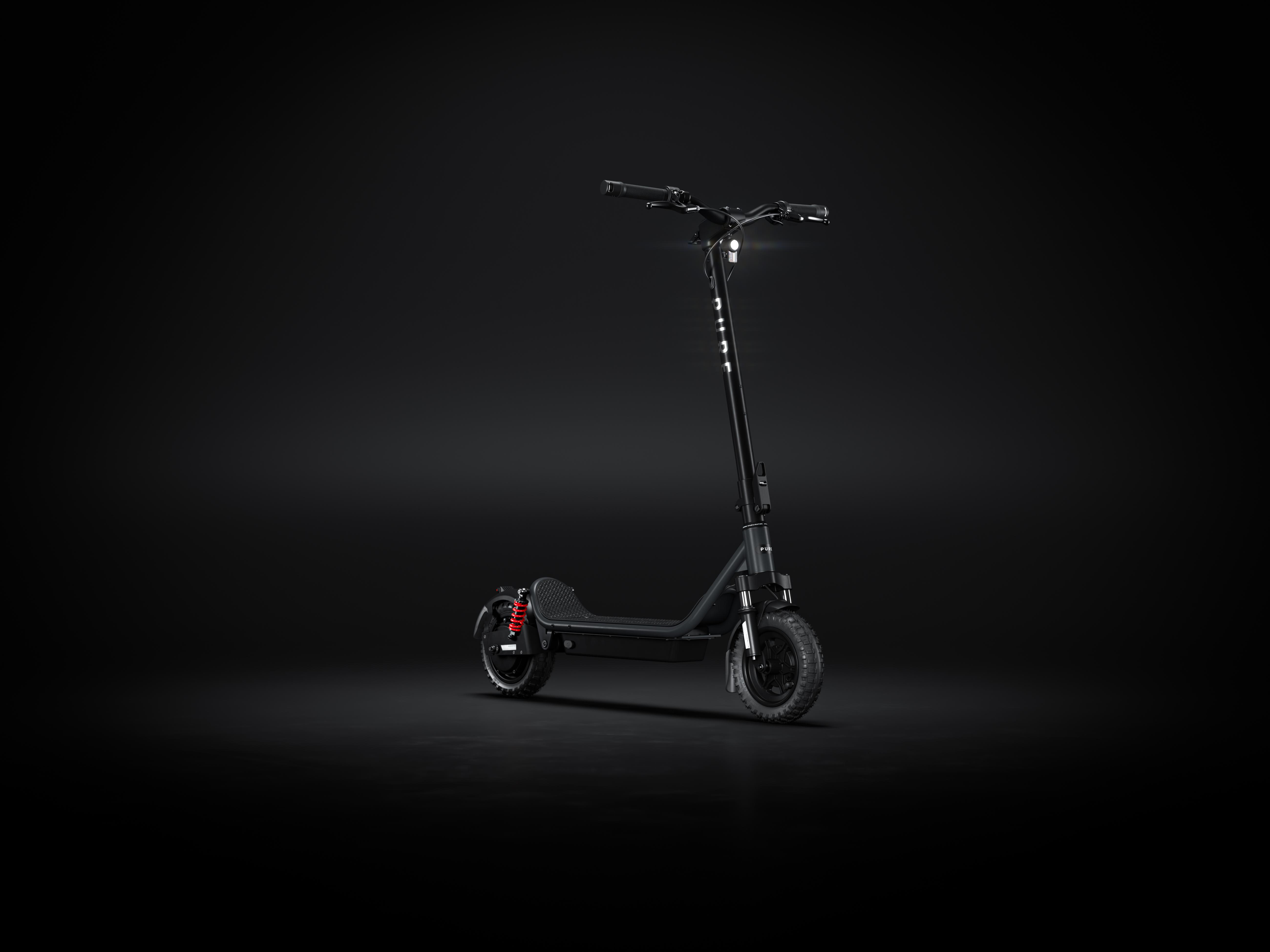 Ein schwarzer E-Scooter mit roten Stoßdämpfern steht im Dunkeln.