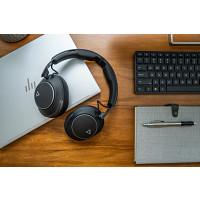 Schwarze Kopfhörer liegen auf einem Laptop neben einer Tastatur und einem Notizbuch.