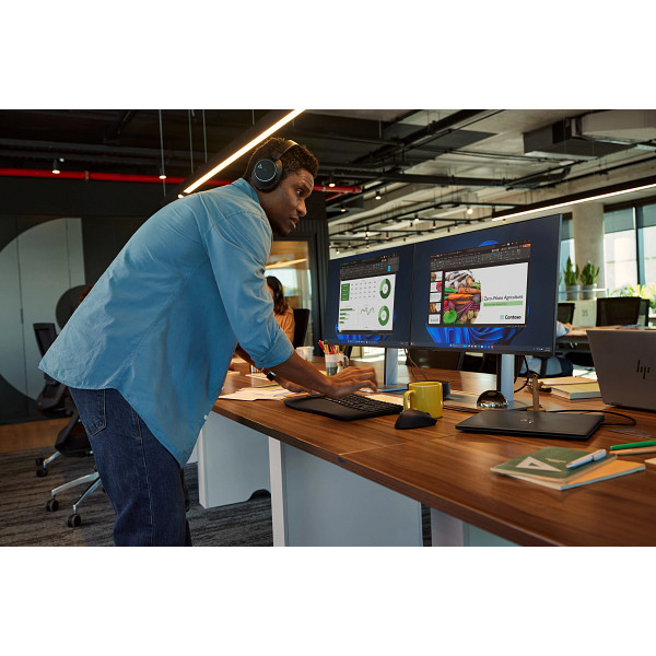 Mann mit Kopfhörern arbeitet an zwei Computermonitoren in einem modernen Büro.