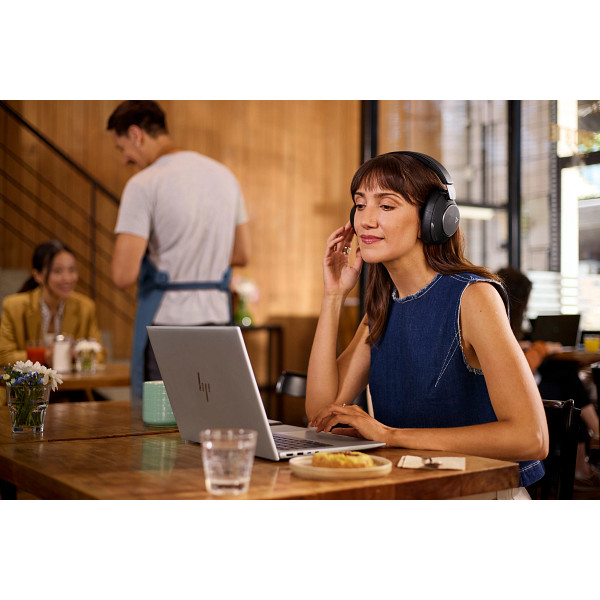 Eine Frau mit Kopfhörern arbeitet in einem Café an einem Laptop, Gebäck und Getränk daneben.