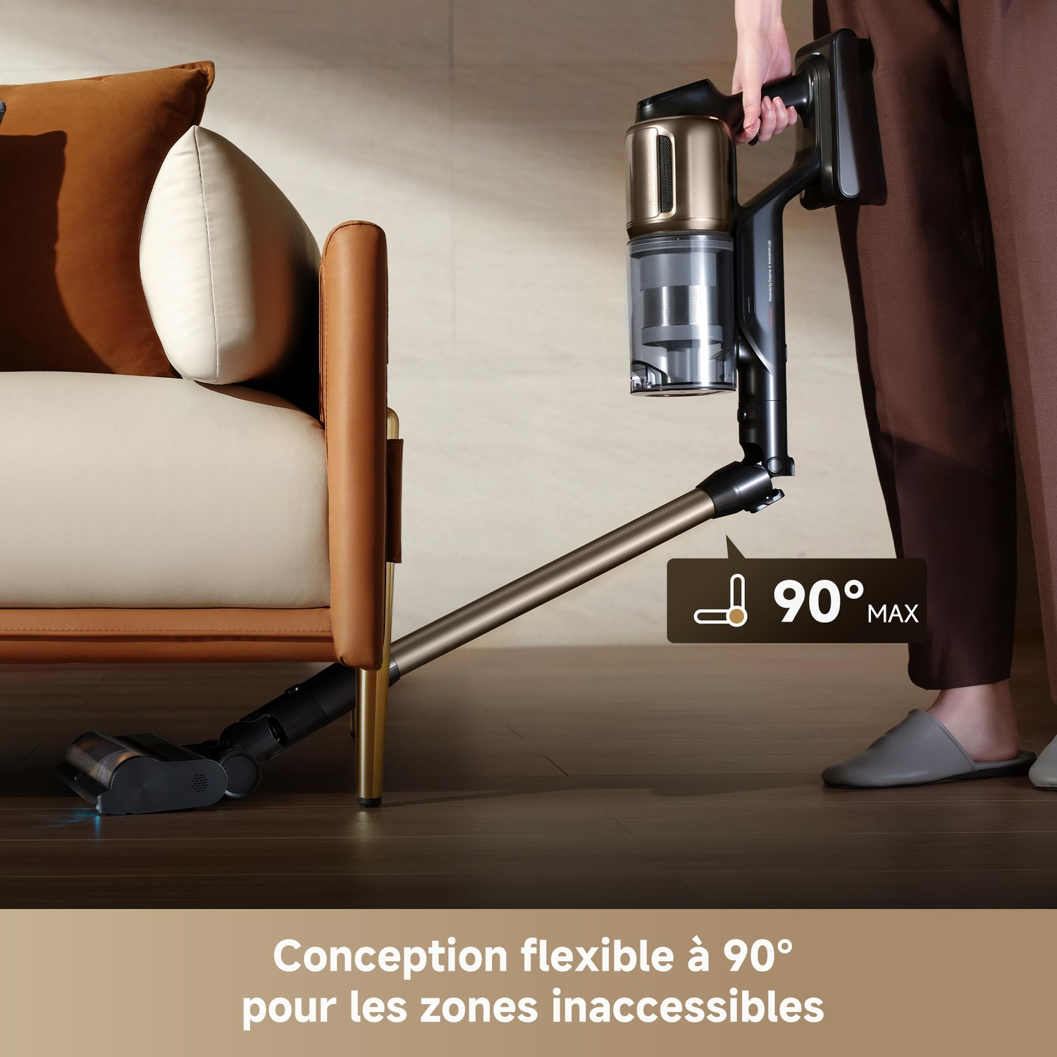 Un aspirateur à main est utilisé au sol près d'un canapé, incliné à 90°.