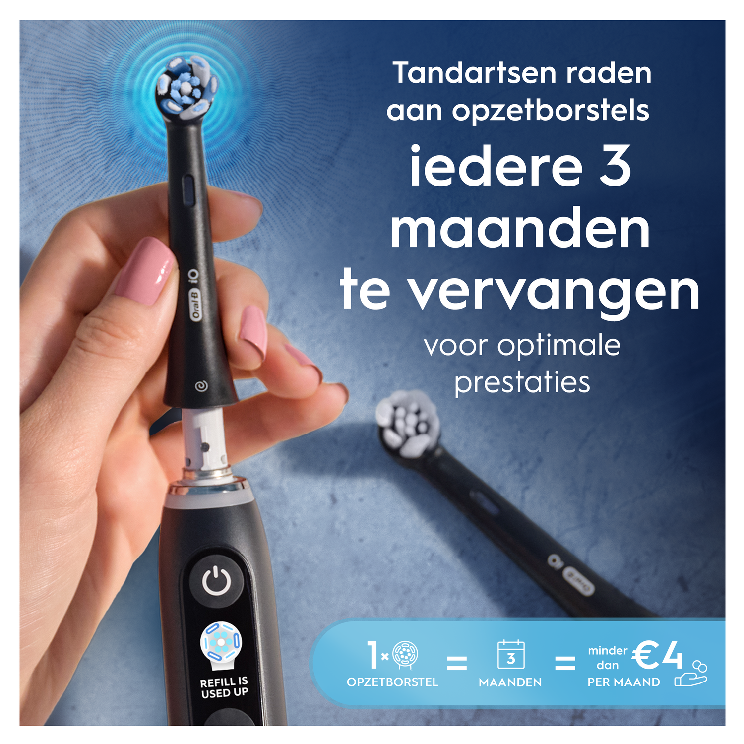 A black electric toothbrush with a head is held by a hand. A replacement head lies nearby.