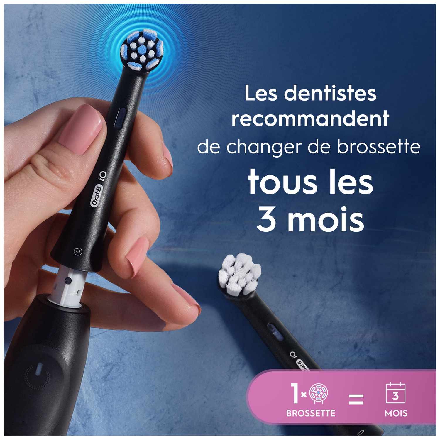 Une main tient une brosse à dents noire avec des poils bleus et blancs. Un autre embout est à côté.