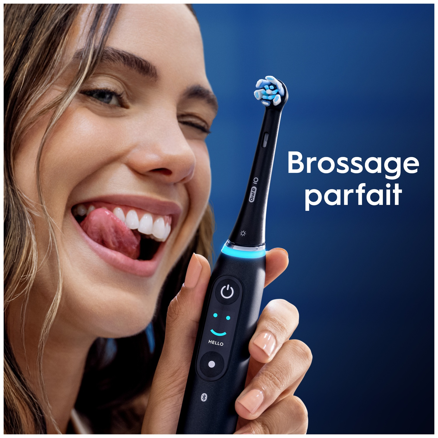 Une femme sourit, montrant ses dents et tenant une brosse à dents électrique noire.