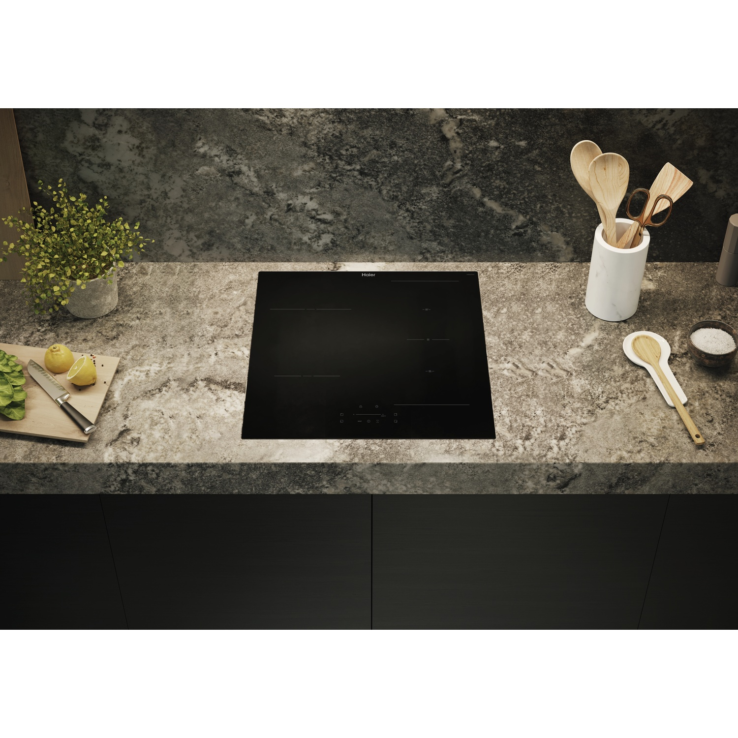 Un piano cottura a induzione nero su un piano di lavoro in marmo con utensili da cucina.