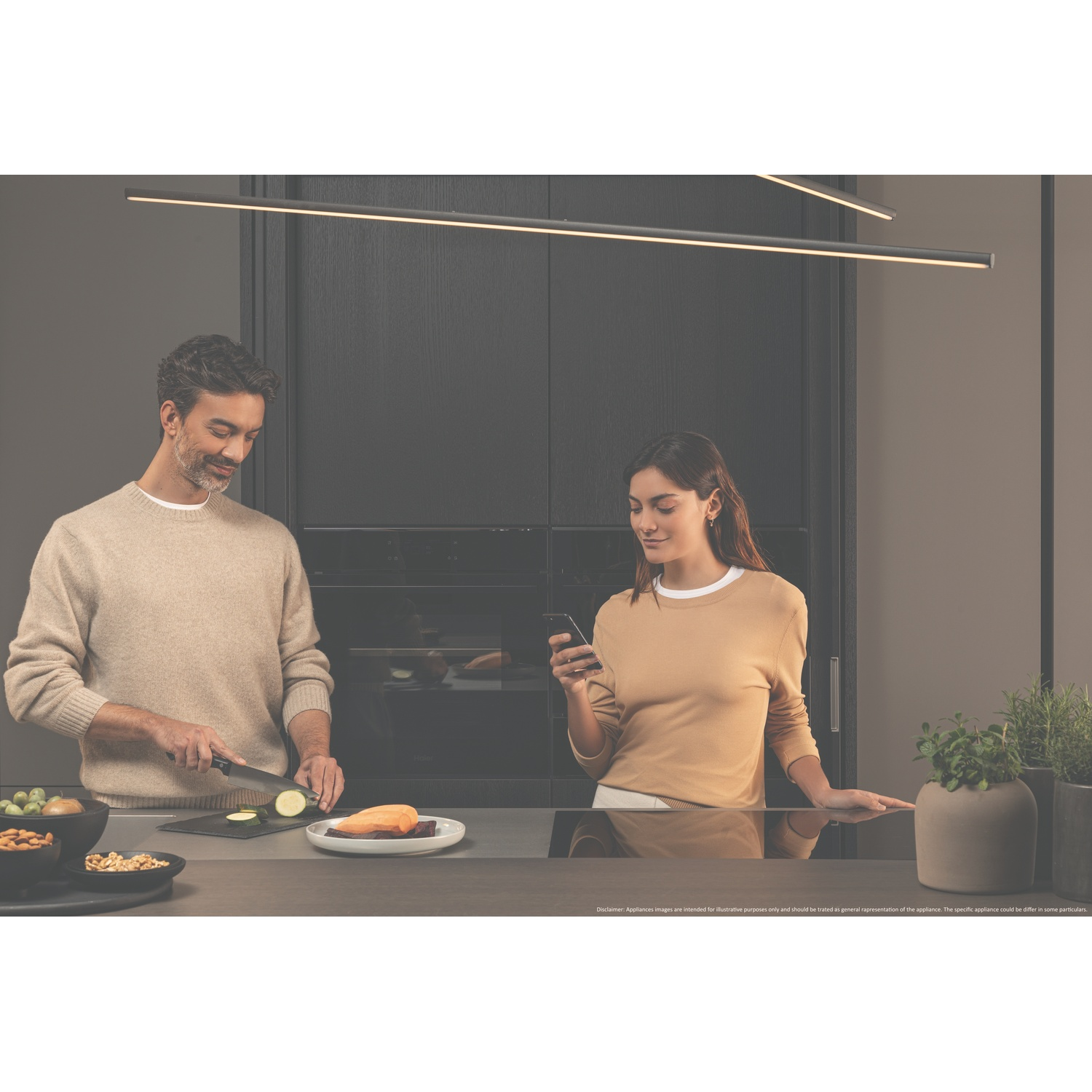 Un uomo taglia zucchine, una donna guarda il telefono in una cucina moderna.