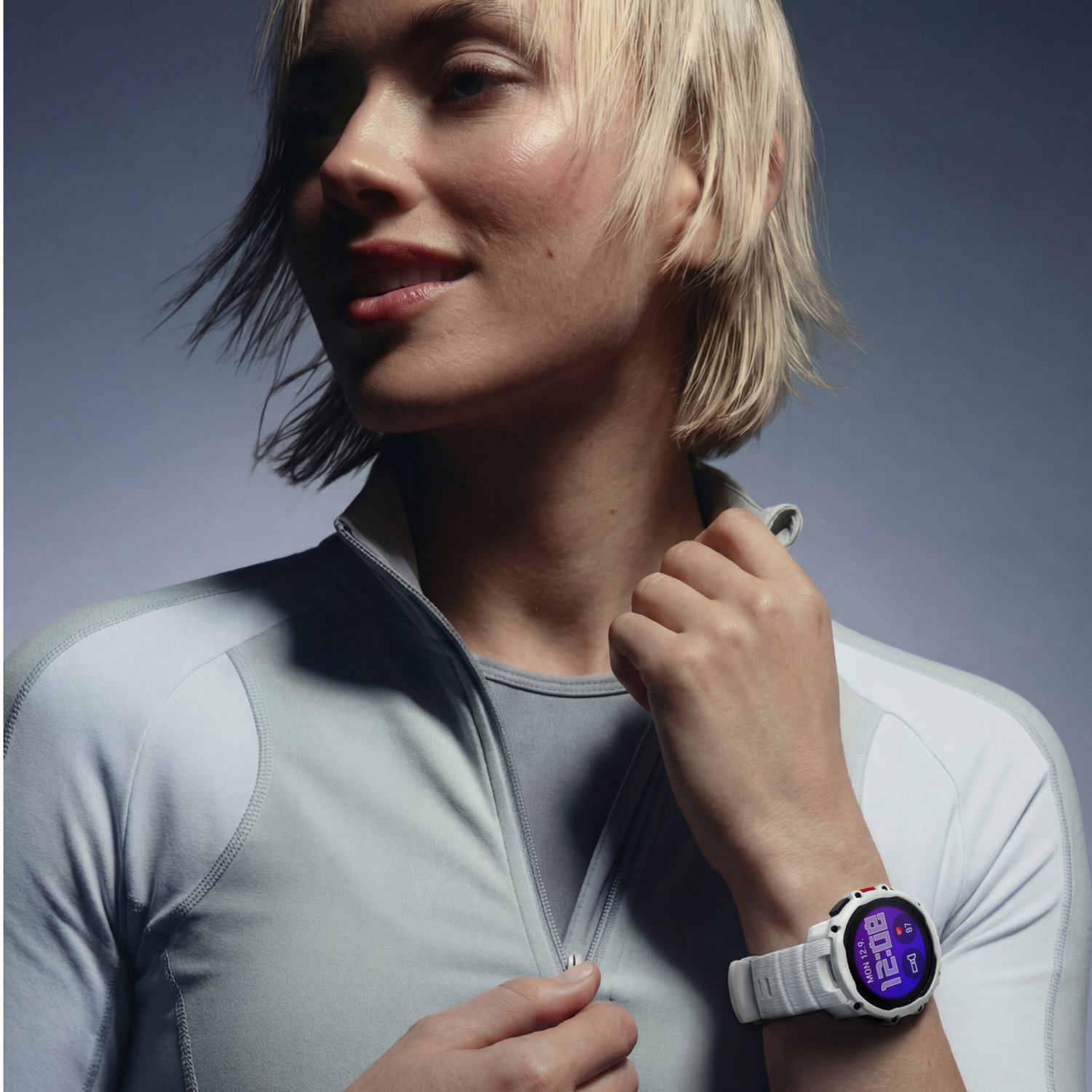 Una mujer de pelo rubio corto lleva una chaqueta deportiva gris y un reloj inteligente.