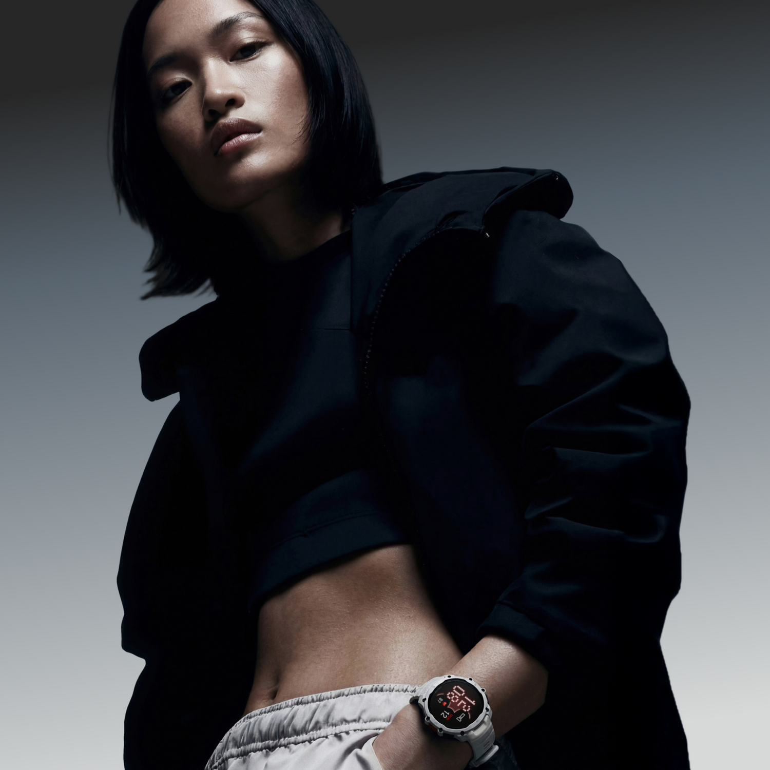 Una mujer con chaqueta negra y pantalones claros lleva un smartwatch blanco. Se le ven los abdominales.