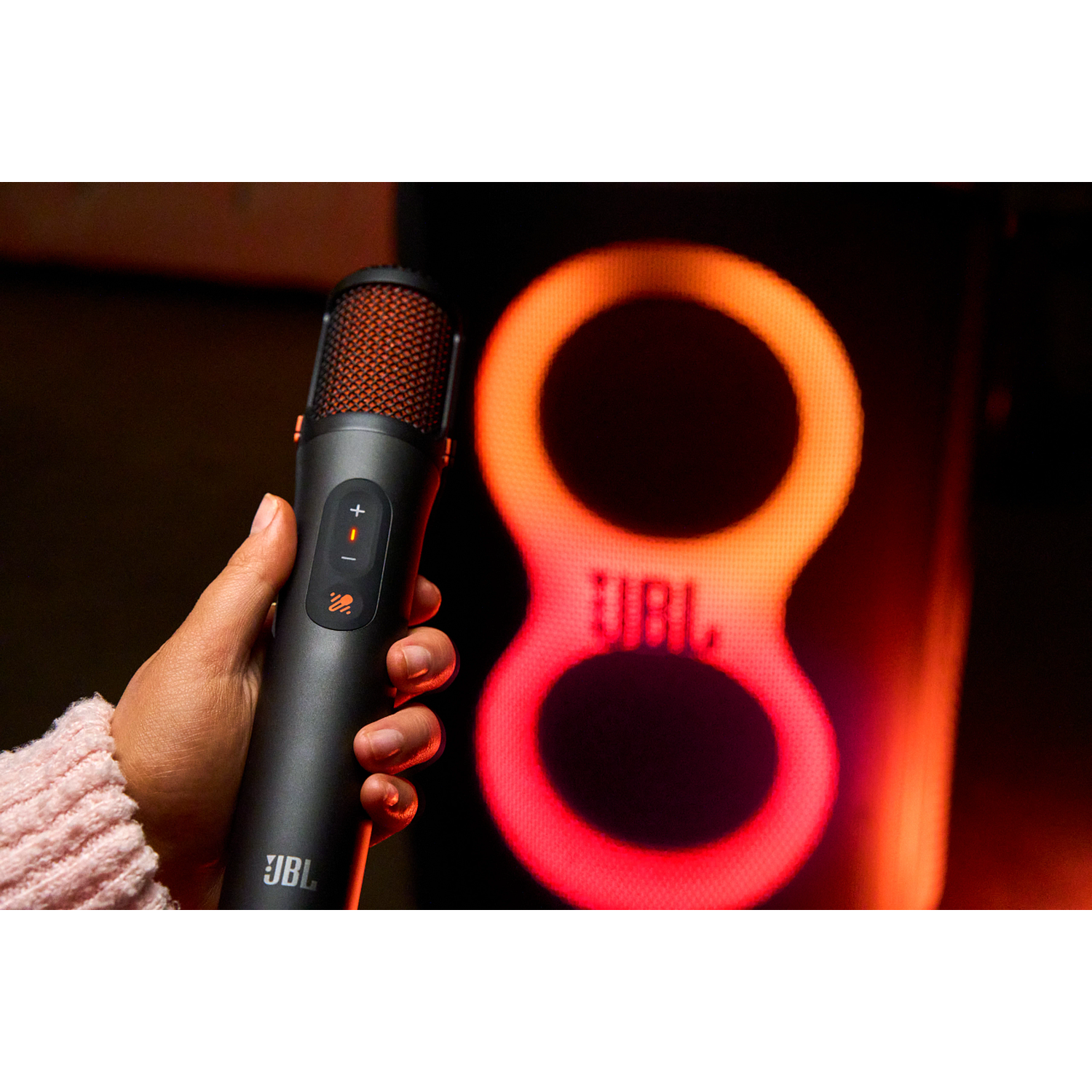 A hand holds a black JBL microphone in front of a glowing, figure-eight light.