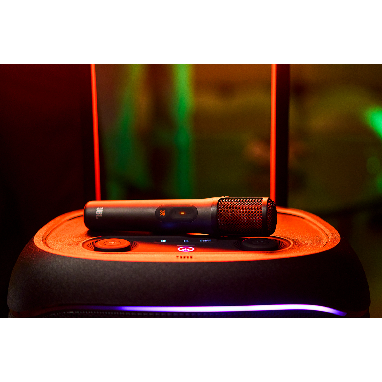A black microphone rests on a JBL speaker with orange lighting.