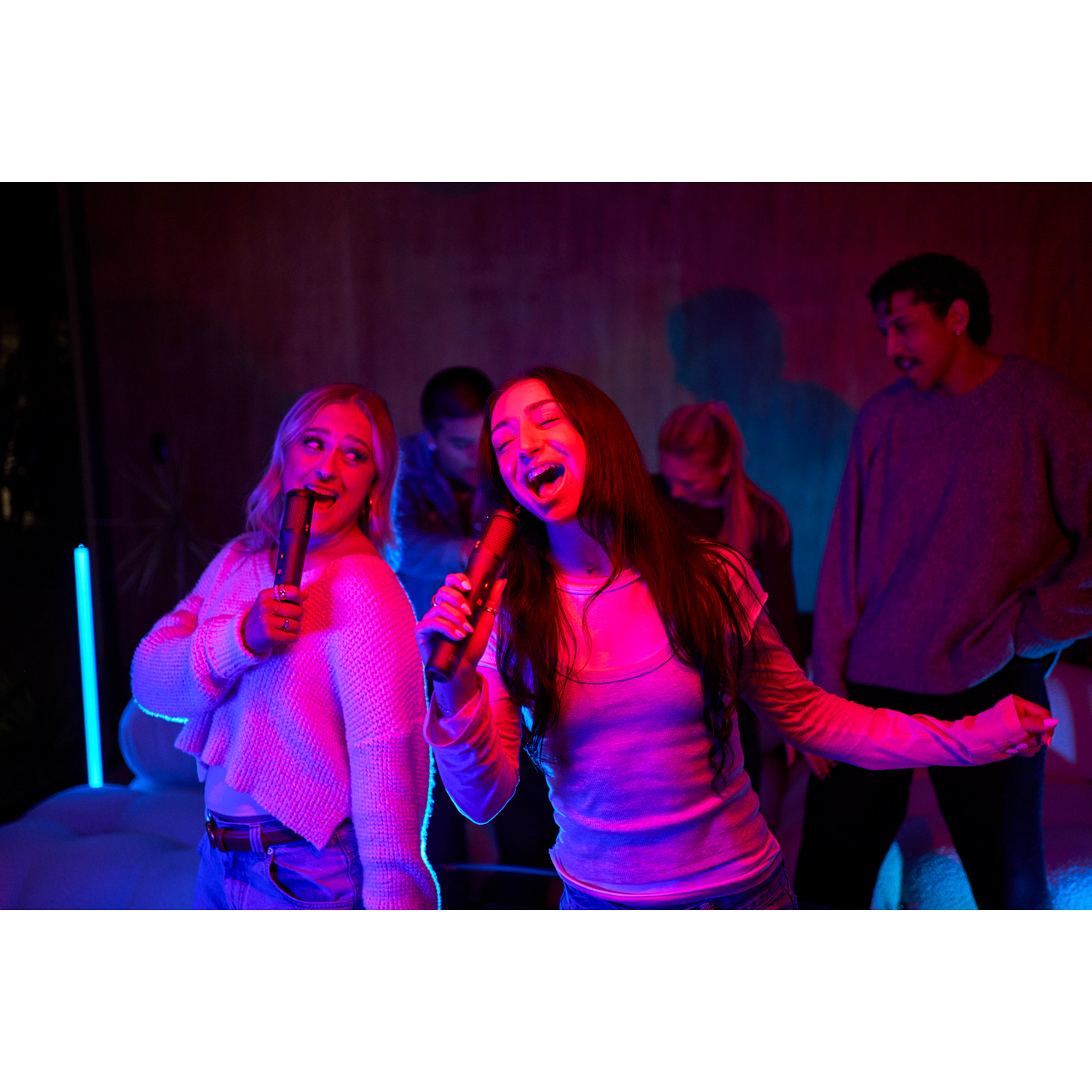 Young people singing with microphones at night, lit by neon lights.
