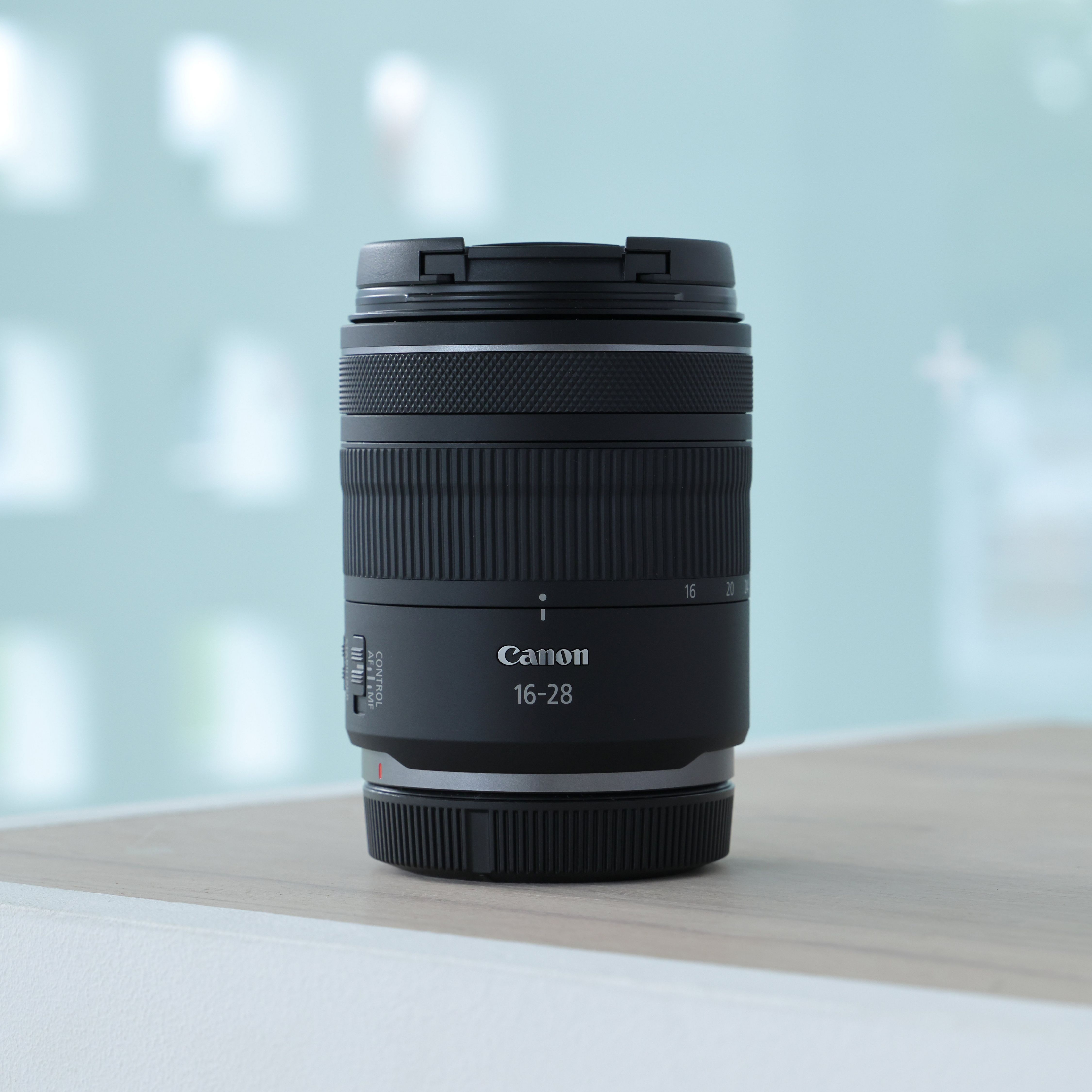 Un objectif Canon 16-28 noir avec une bague de mise au point repose sur une table en bois.